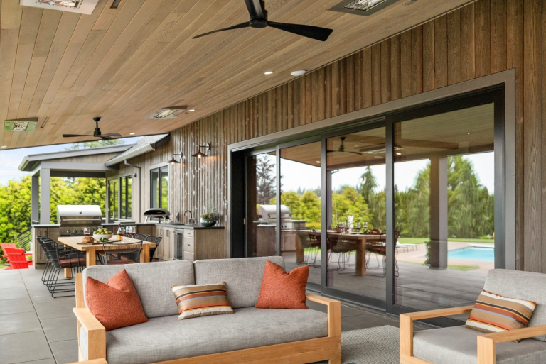 An outdoor living room, kitchen, and dining space featuring a large siding glass door