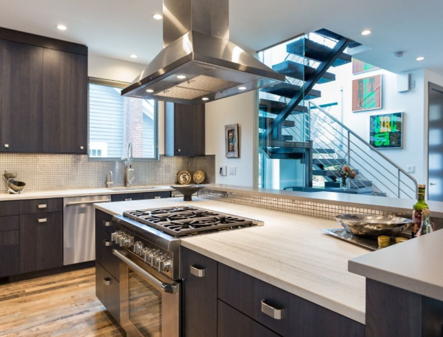 A 3-story floating wood and stainless staircase, showcased by oversized windows and dramatic lighting. Walnut cabinetry with a distinct stain and natural slab surfaces in the kitchen offset the metals used throughout the opened space.