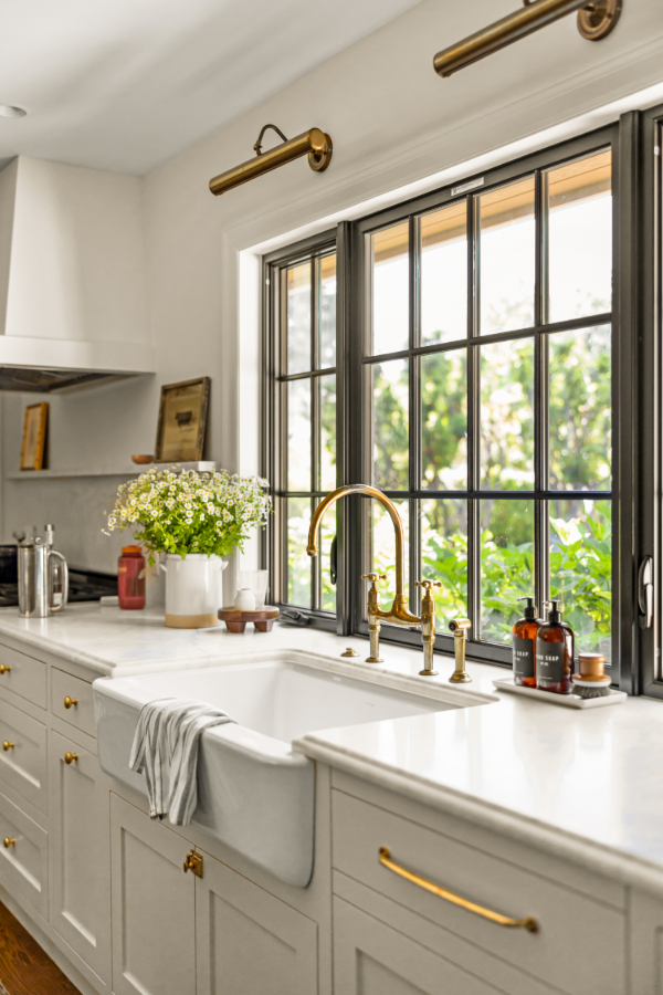 A new luxury kitchen with a farmhouse sink, white cabinets and counter, and gold fixtures and hardware to help illustrate how to survive a kitchen remodel.