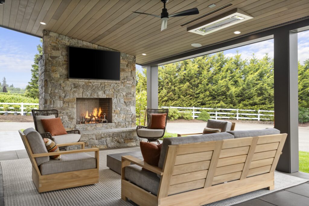 Image of an outdoor living area, complete with cover, heating element, fireplace, TV, and sitting area to help illustrate Does Outdoor Living Space Add Value