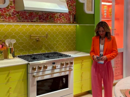 A woman wearing bright colors in a kitchen design presentation featuring range hood, oven, countertops, and more in a variety of colors.